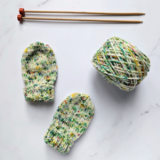 Single-point wooden needles, a cake of hand-dyed yarn and a pair of baby mitts.
