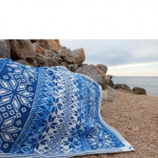 Scandinavian motif overlay mosaic blanket in blue and white spread over a rock at the shore.