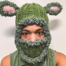 Green balaclava has sideways, Shrek-stye ears. Openings, ears and face covering are trimmed in fuzzy yarn.