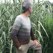 Man in knitted pullover that has crew neck, long sleeves and is divided into six wide stripes.