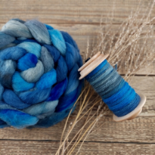 Coiled braid of bright blue, light blue and gray roving, next to a spindle with sample yarn spun from it.
