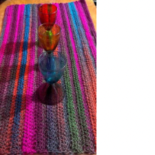 Table runner crocheted horizontally in deep colors and fluorescents. Shown with three colorful goblets.