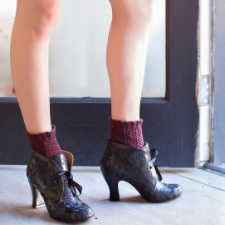 Woman in sunny doorway wears high-heel short boots. Textured boot cuff extends into boot and ends in a stirrup.