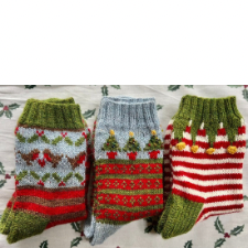 Three pairs of Christmas theme socks. One has holly and turtledove motifs, then stripes. The second has Christmas trees and decorative stripes. The last has red and white stripes, then a colorwork elf-like triangles that come down with gold bobbles for jingle bells.