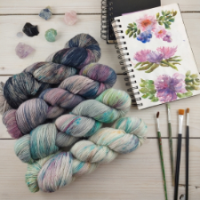 Four variegated skeins from light to dark. Light skeins are blues, greens and white. Darks are purples and black.