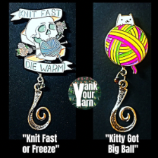 Two Portuguese knitting pins. One has an old-school tattoo style enamel pin with a skull that says, Knit Fast, Die Warm. The other is a cat clinging to a giant yarn ball and is called Kitty Got Big Ball.