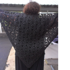 Woman stretches arms to show triangular shawl made of crocheted skulls.