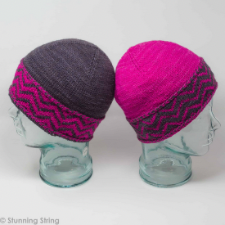 Two beanies with colorwork and Latvian braid on the brim. First hat is hot pink with charcoal zig zags on the brim. Second hat swaps the two colors.