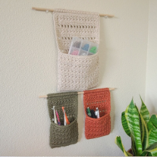 Large pocket and two smaller pockets hung on the wall using dowels. Small pockets hold pens and crochet hooks. Larger pocket holds a divided organizer.