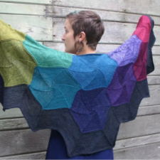 Triangular knitted shawl where every large hexagon is a different color. Bottom border is a dark neutral zigzag.