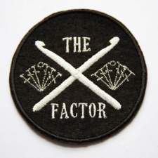 X Factor patch has crossed crochet hooks for the X, flanked by crochet chart excerpts.