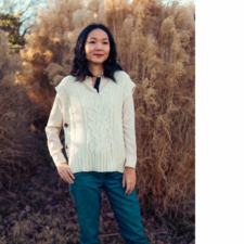 Woman in a field in the fall, wearing a pullover V-neck cabled vest that buttons down the sides.