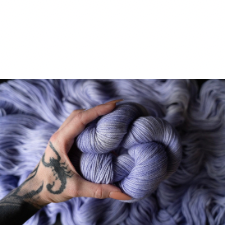 Tattooed hand holds tonal lavender yarn with hints of silver.