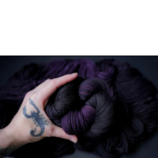 Tattooed hand holds purple and black variegated yarn.
