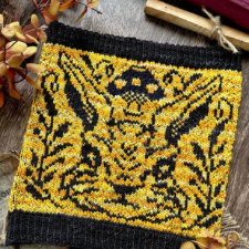 Colorwork of very serious bunny head takes up entire side of cowl. It is flanked by two plants. Above its head is a spotted mushroom. Colorwork is black on variegated yellow background.