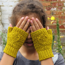 Child covers her eyes while wearing fingerless mitts with large, clear hearts on a textured background. Thumb, finger opening and cuffs have ribbing.