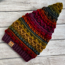 Hat in different textures and colors is shaped at the bottom like a beanie but curves upward into into a tall point.