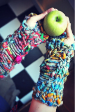 Two hands in brightly colored single-ply handspun cradle a green apple.